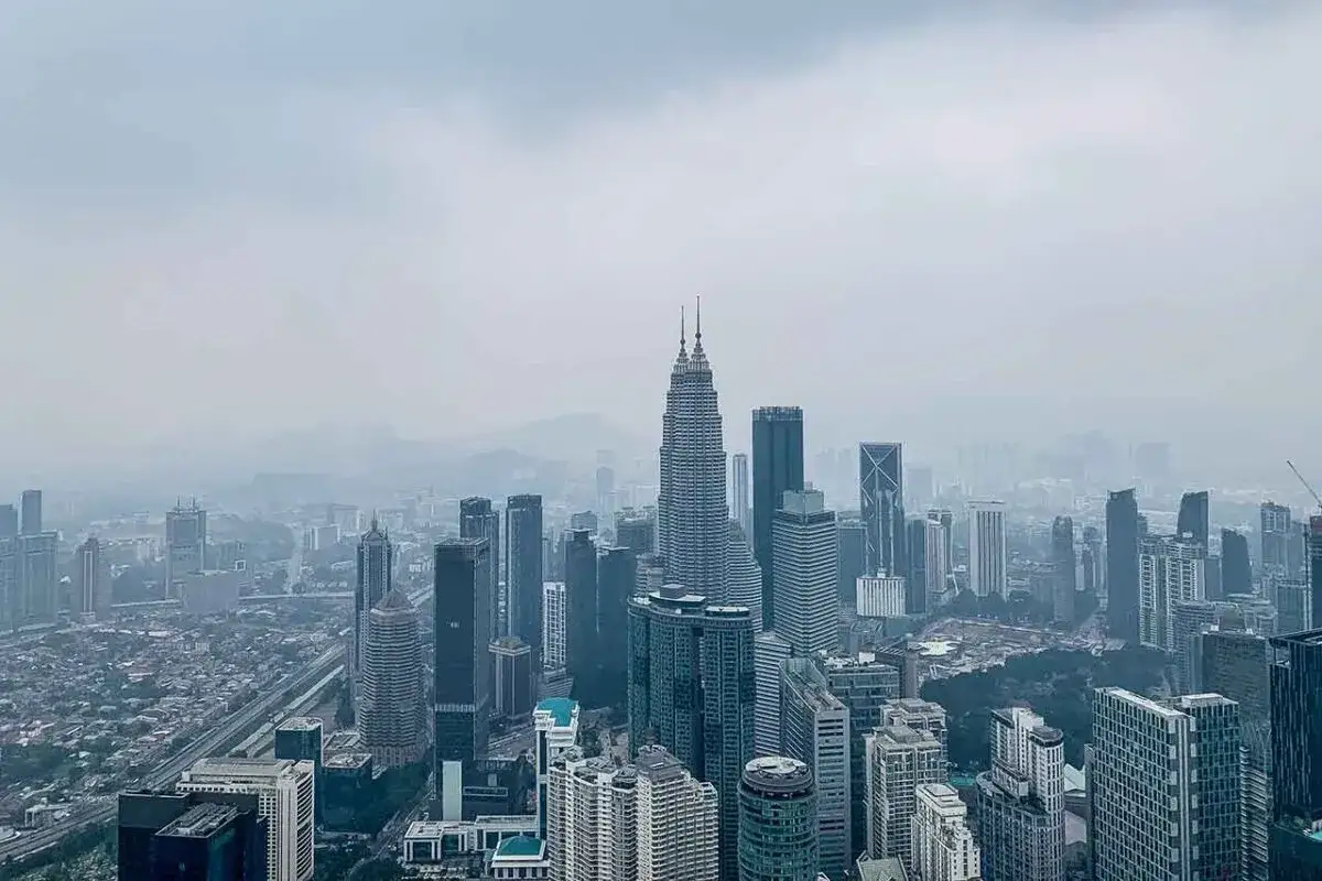 Widok na drapacze chmur w Kuala Lumpur, stolicy Malezji, w mglisty dzień. W centrum dominują bliźniacze wieże Petronas.