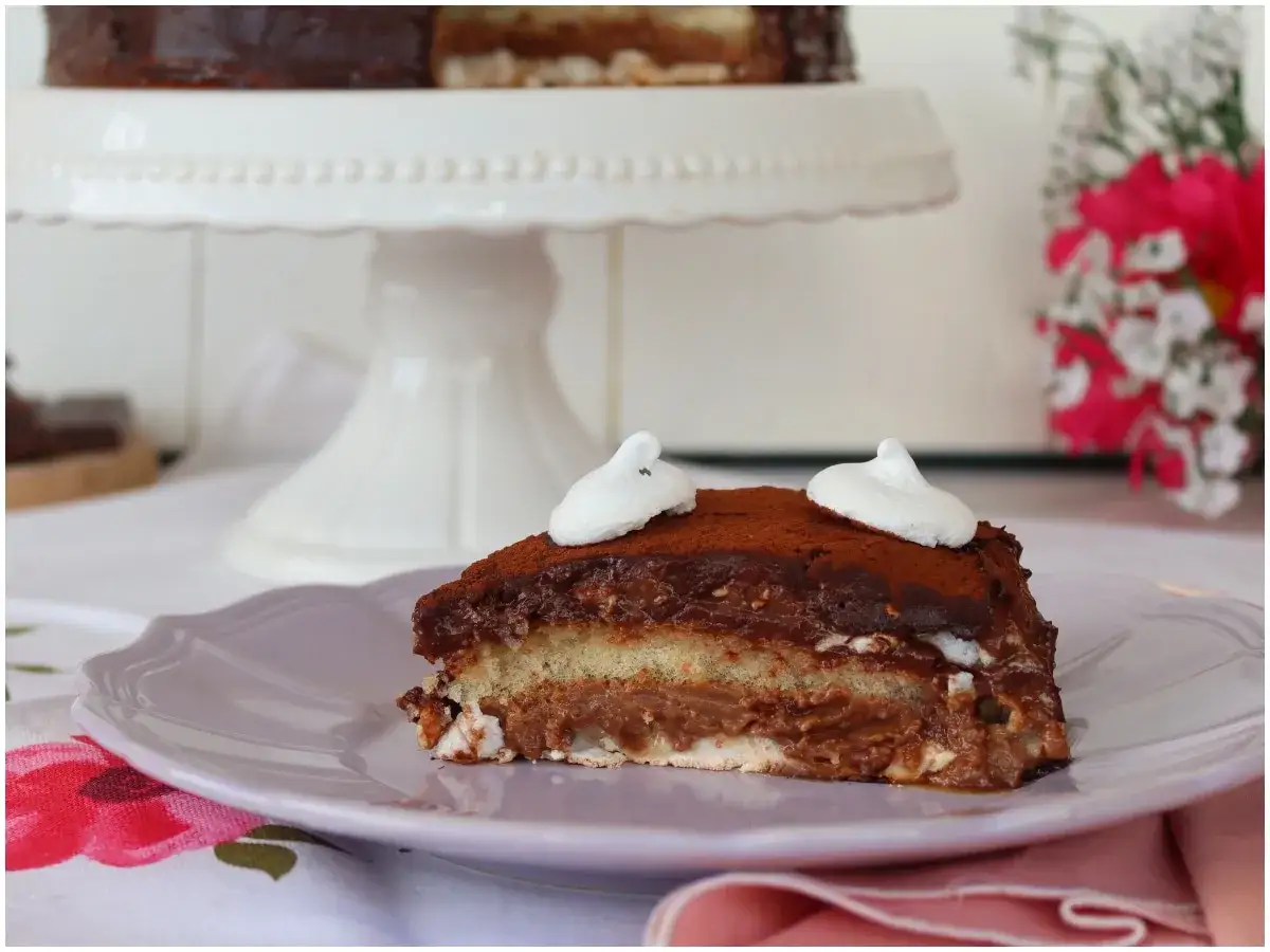 Una fetta di meringata al cioccolato, con strati di pan di Spagna, crema al cioccolato e meringa, decorata con cacao e meringhette.