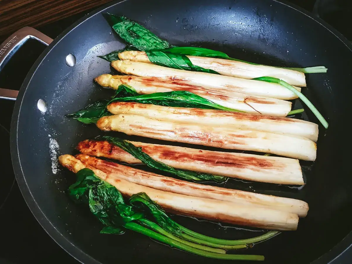 Asperges blanches poêlées dans une poêle, avec des feuilles vertes. Un plat simple et savoureux.