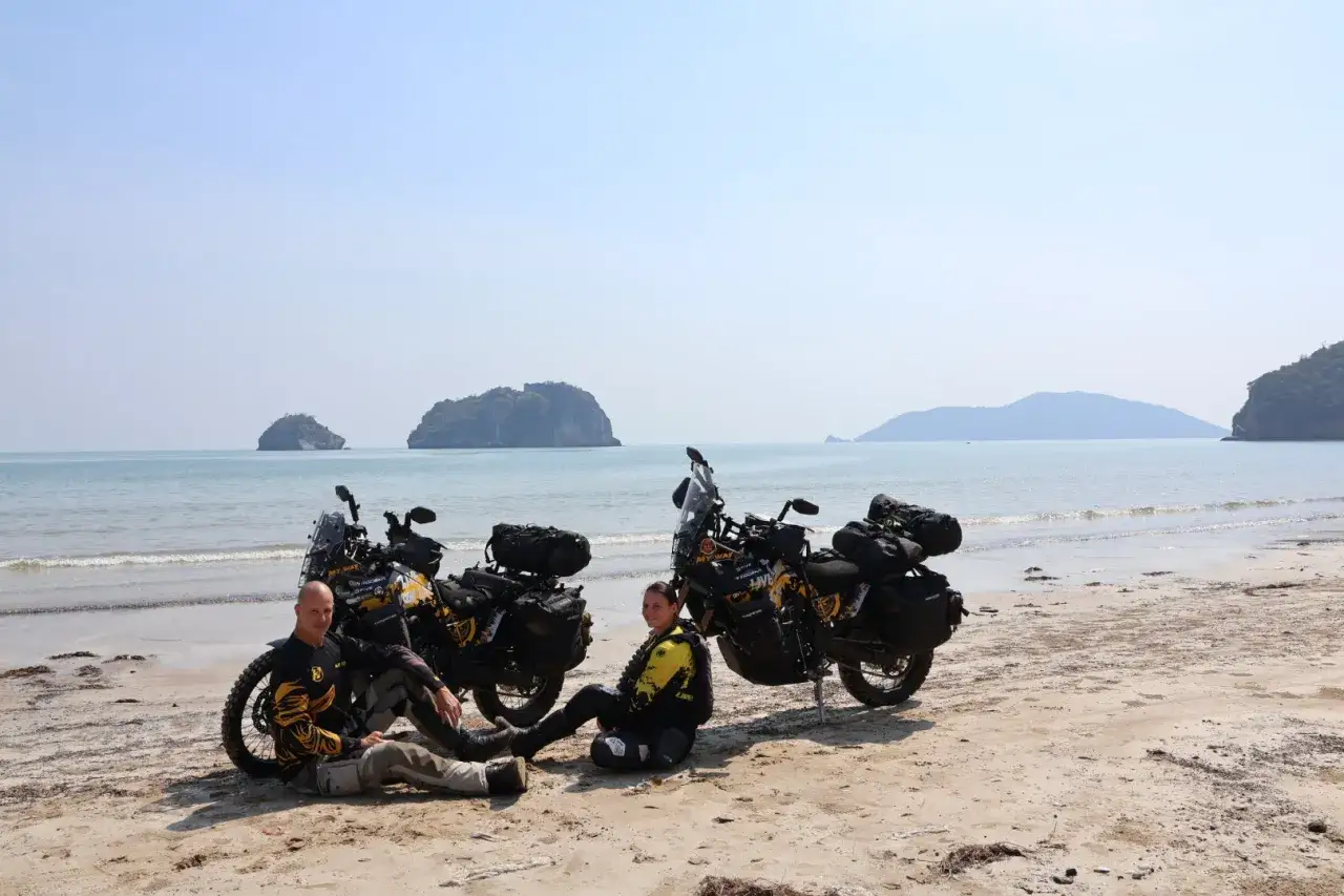 Dwie pary siedzą na plaży obok swoich motocykli, gotowi na podróż motocyklem nad morze.