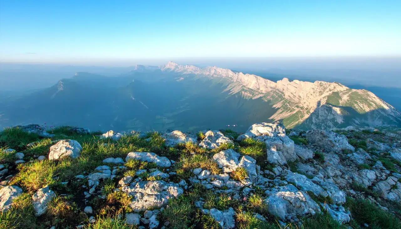 Vue panoramique depuis le plateau Ambel, avec des montagnes majestueuses baignées par la lumière du soleil levant.