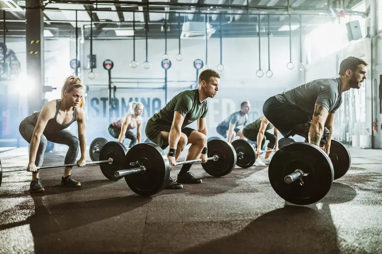 Ludzie ćwiczą podnoszenie ciężarów w siłowni. To właśnie crossfit co to – trening siłowy i kondycyjny w grupie.