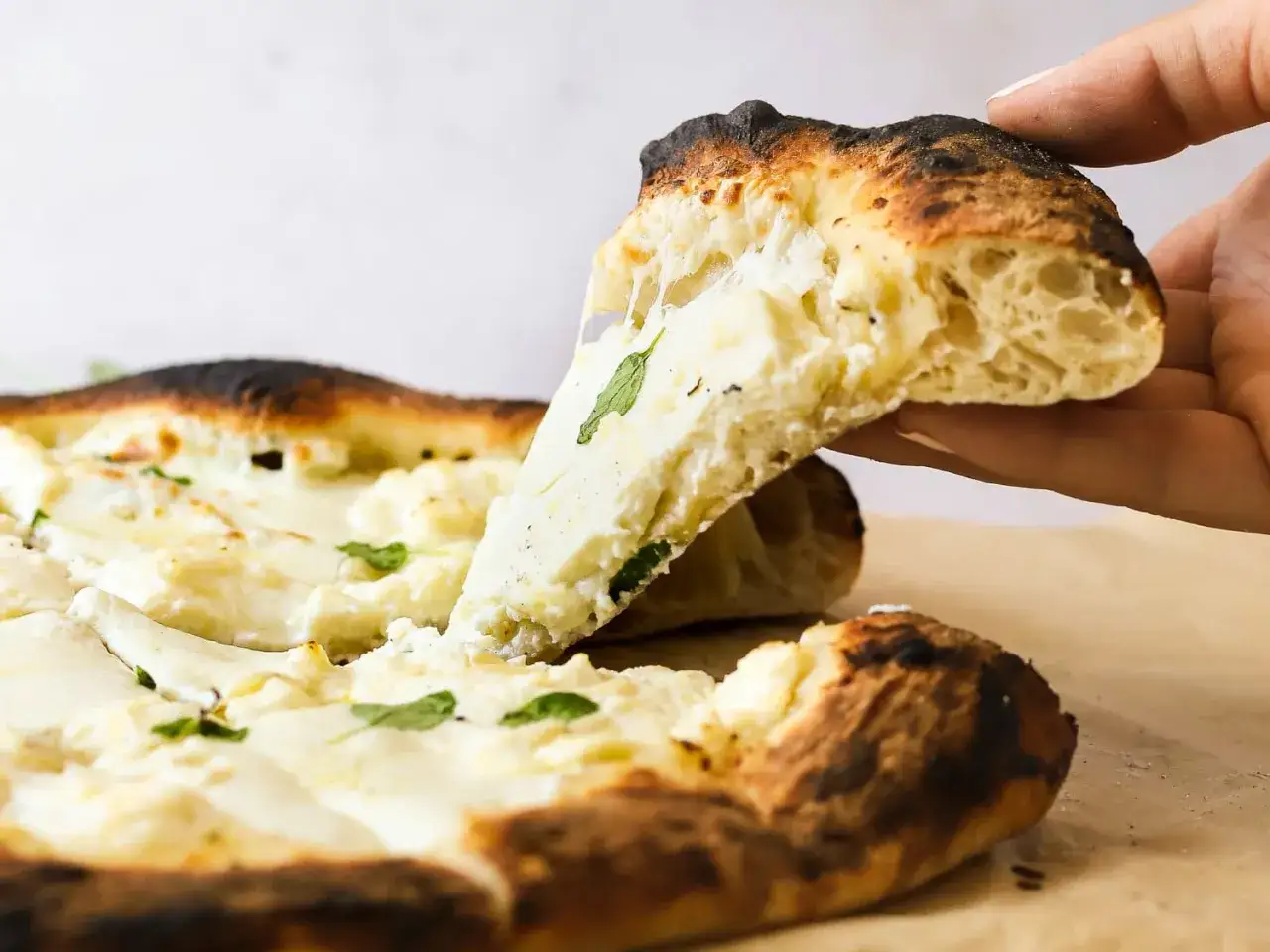 En hand lyfter en bit av en kr&auml;mig pizza bianco, perfekt f&ouml;r ett enkelt pizza bianco recept.