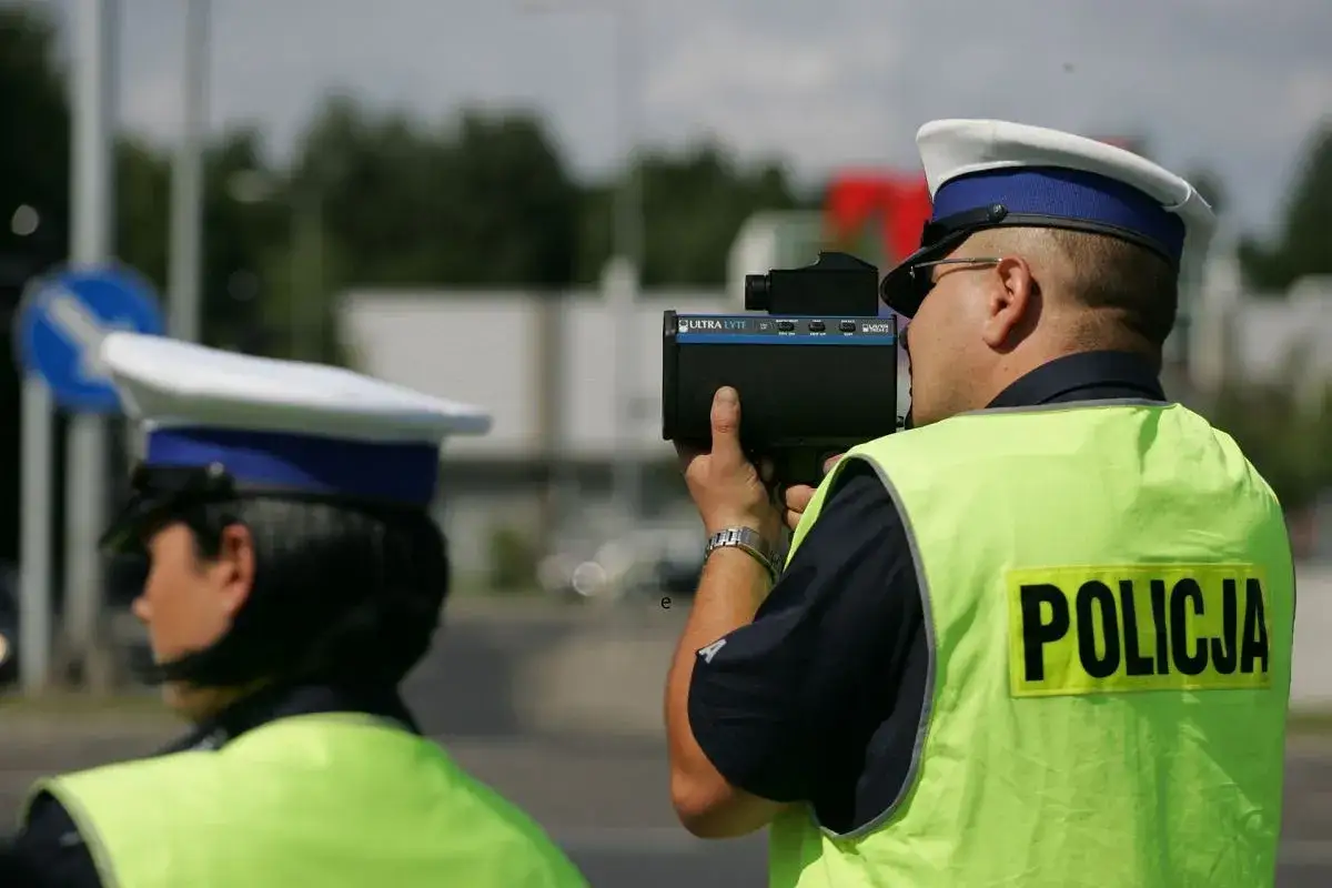 Policjant w kamizelce odblaskowej mierzy prędkość pojazdów. Dba o bezpieczeństwo na drodze, kontrolując prowadzenie pojazdu.