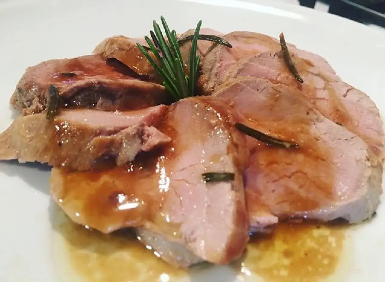 Succulento filetto di maiale in padella, tagliato a fette e nappato con un sugo aromatico, guarnito con rosmarino fresco.