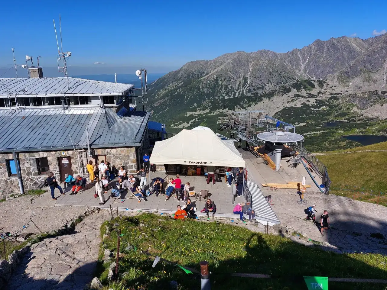 Ludzie odpoczywają przy górnej stacji kolejki na Kasprowy Wierch. W tle piękne Tatry.