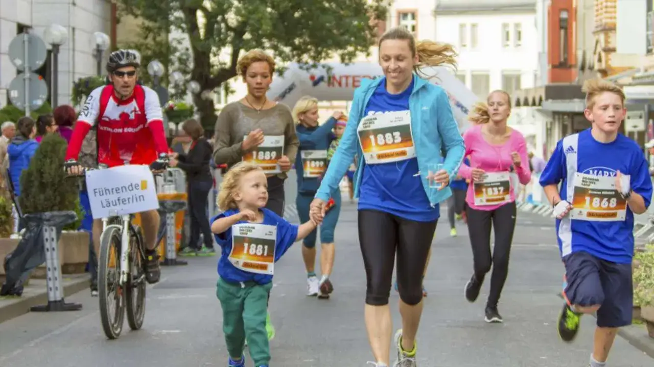 Familien beim Sommernachtslauf Limburg. Ein Radfahrer f&uuml;hrt, w&auml;hrend eine Mutter mit ihrem Kind und andere L&auml;ufer die Strecke entlang rennen.