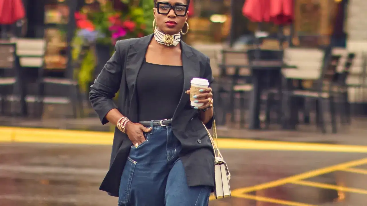 Stylische Frau mit Kaffee und Statement-Schmuck. Ihre weiten Jeans zeigen, welche Jeans sind in: l&auml;ssig und modisch.