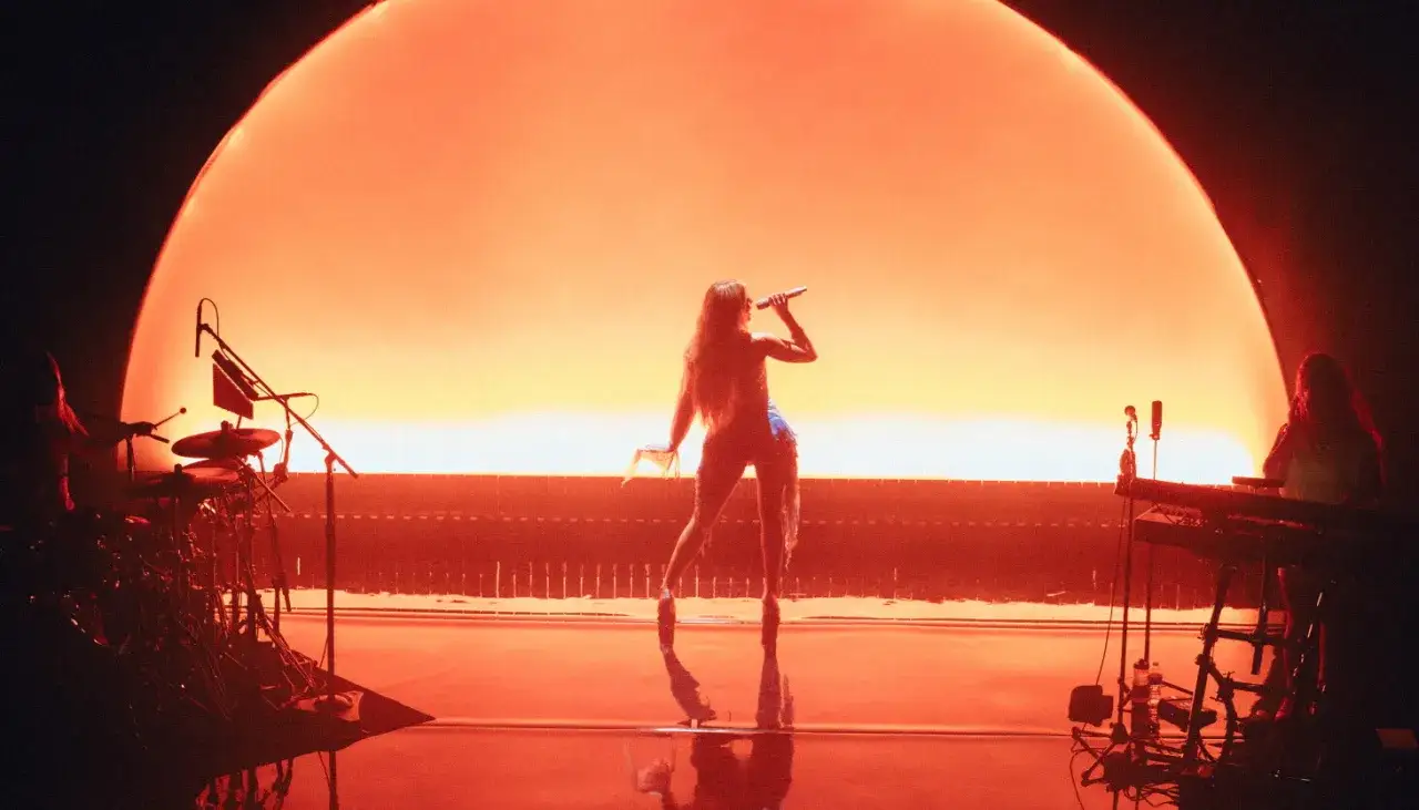 Zara Larsson på scen med en stor orange bakgrund. Hennes framgångar speglas i hennes zara larsson net worth.
