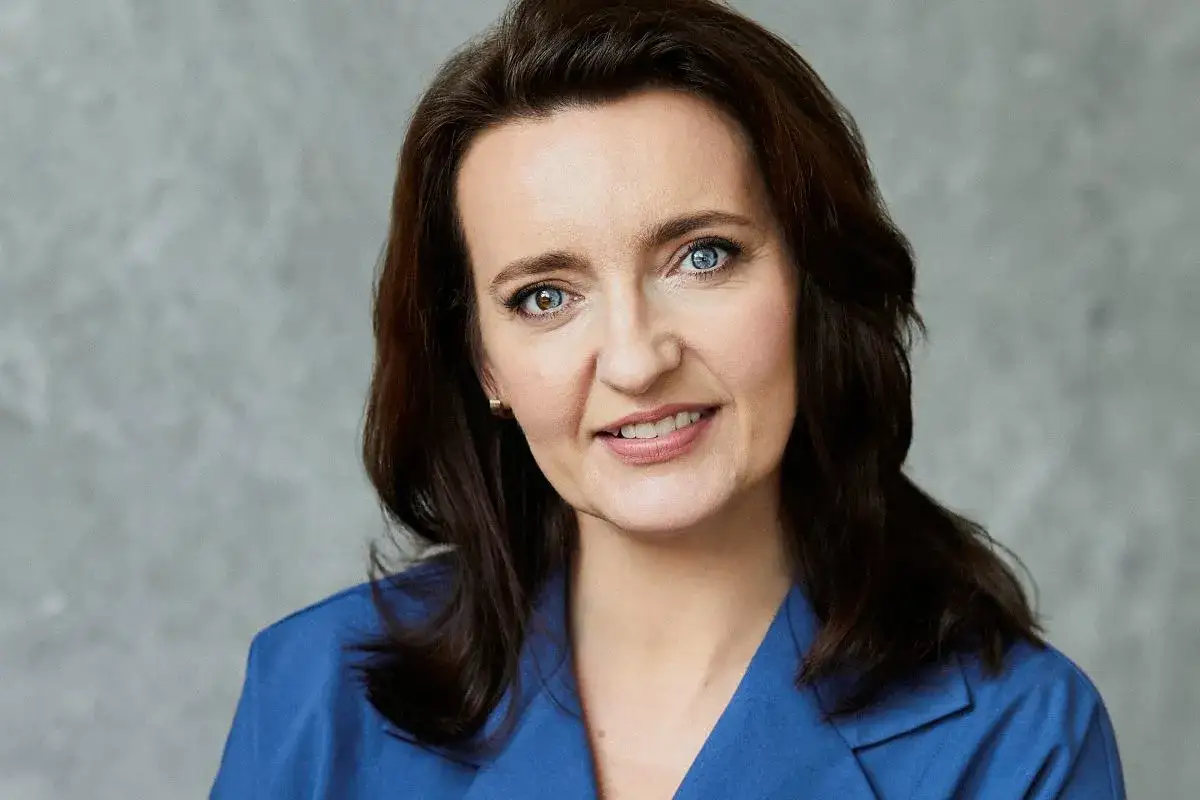 Marzena Okła-Drałowicz, kobieta z dwukolorowymi oczami, w niebieskiej marynarce, uśmiecha się.