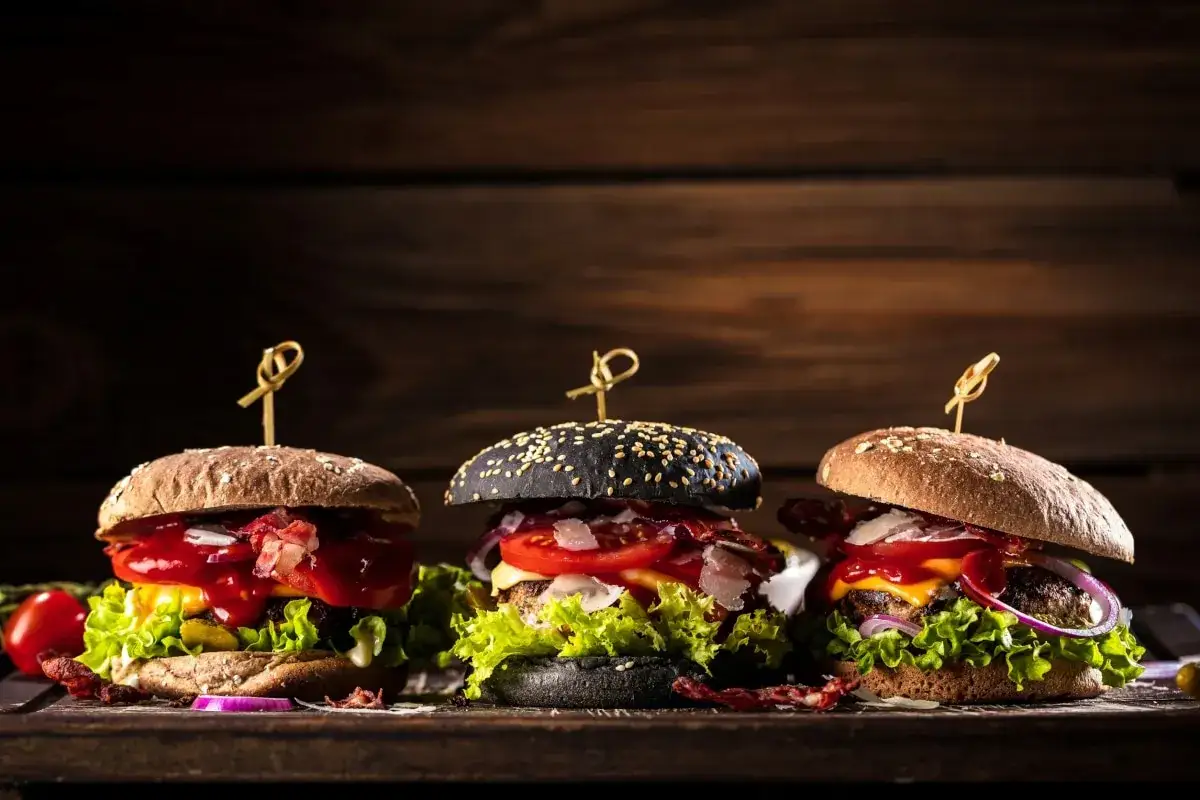 Drei saftige Burger mit verschiedenen burger buns, darunter ein schwarzer, auf einem Holztisch.