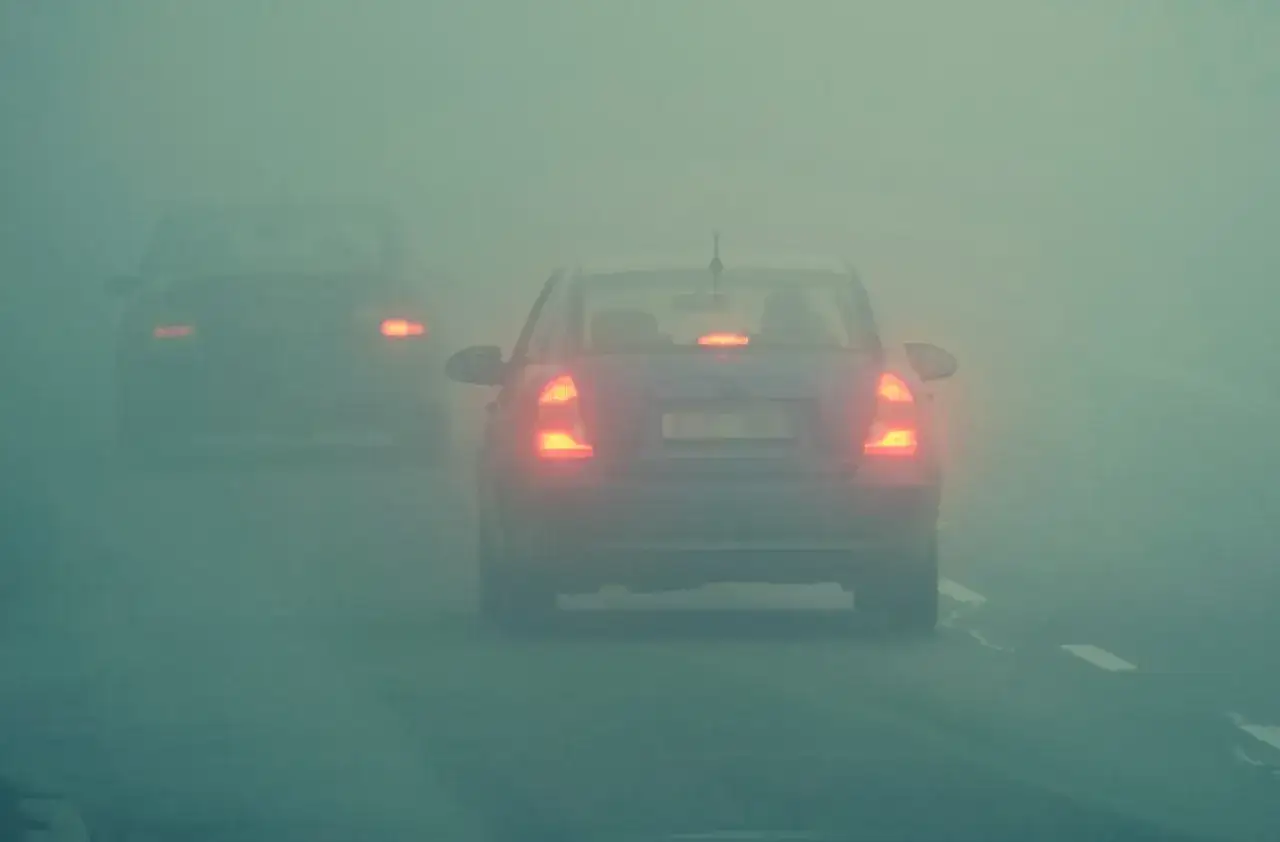 Samochody jadą we mgle, włączone światła przeciwmgielne pomagają widzieć drogę.