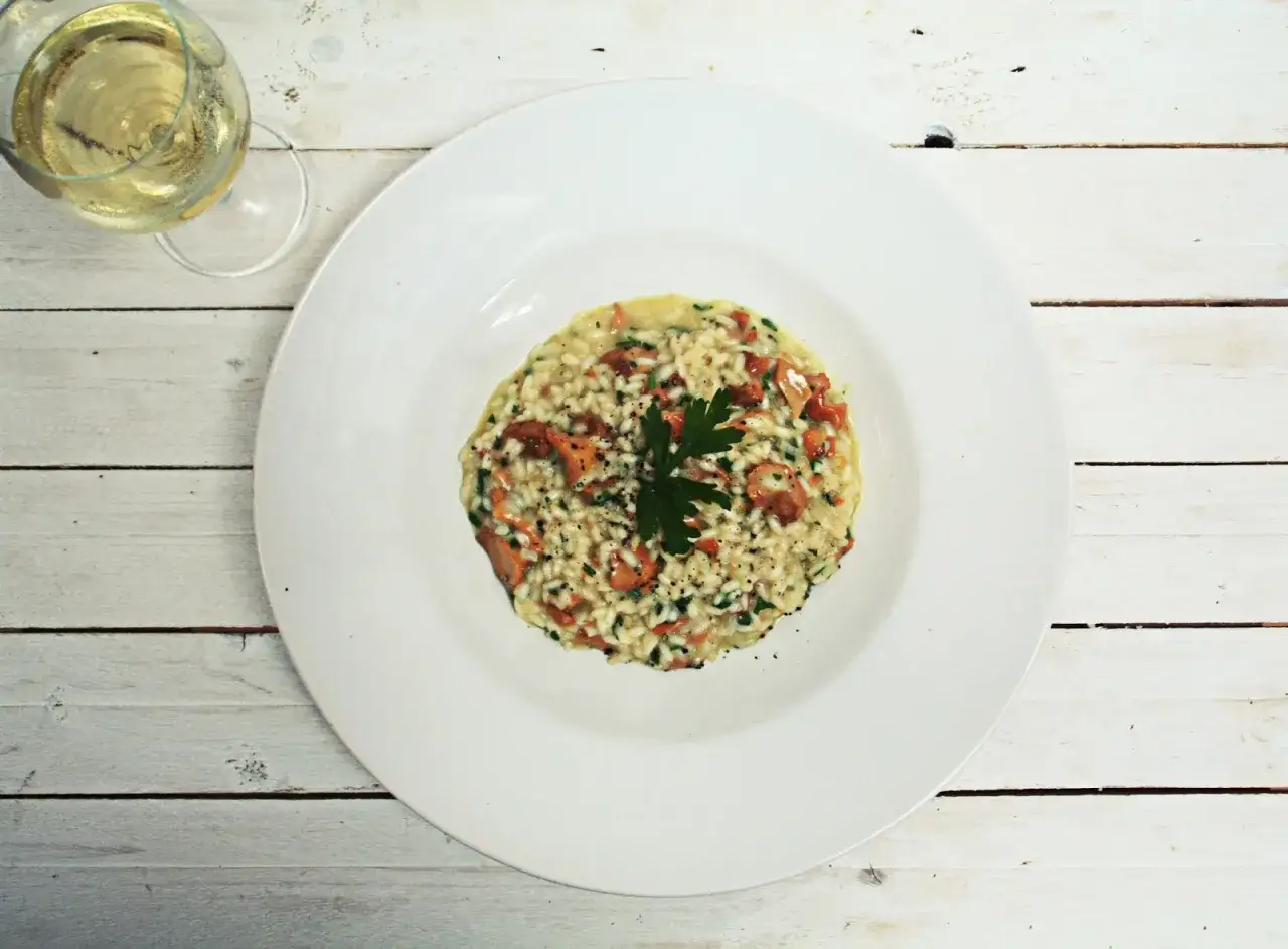 Pyszne risotto z grzybami na białym talerzu, obok kieliszek białego wina. Idealne pytanie: jakie wino do risotto?