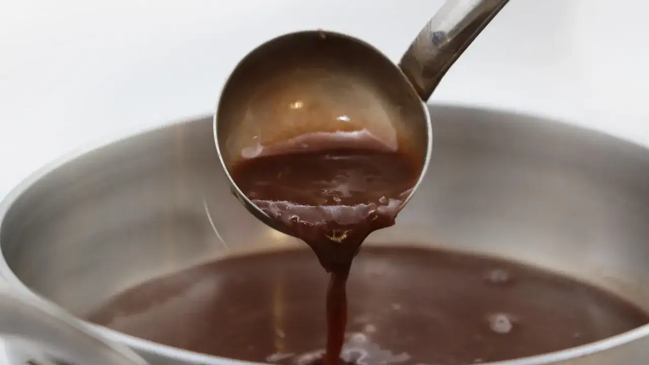 Une louche verse une sauce viande rouge onctueuse dans une casserole.