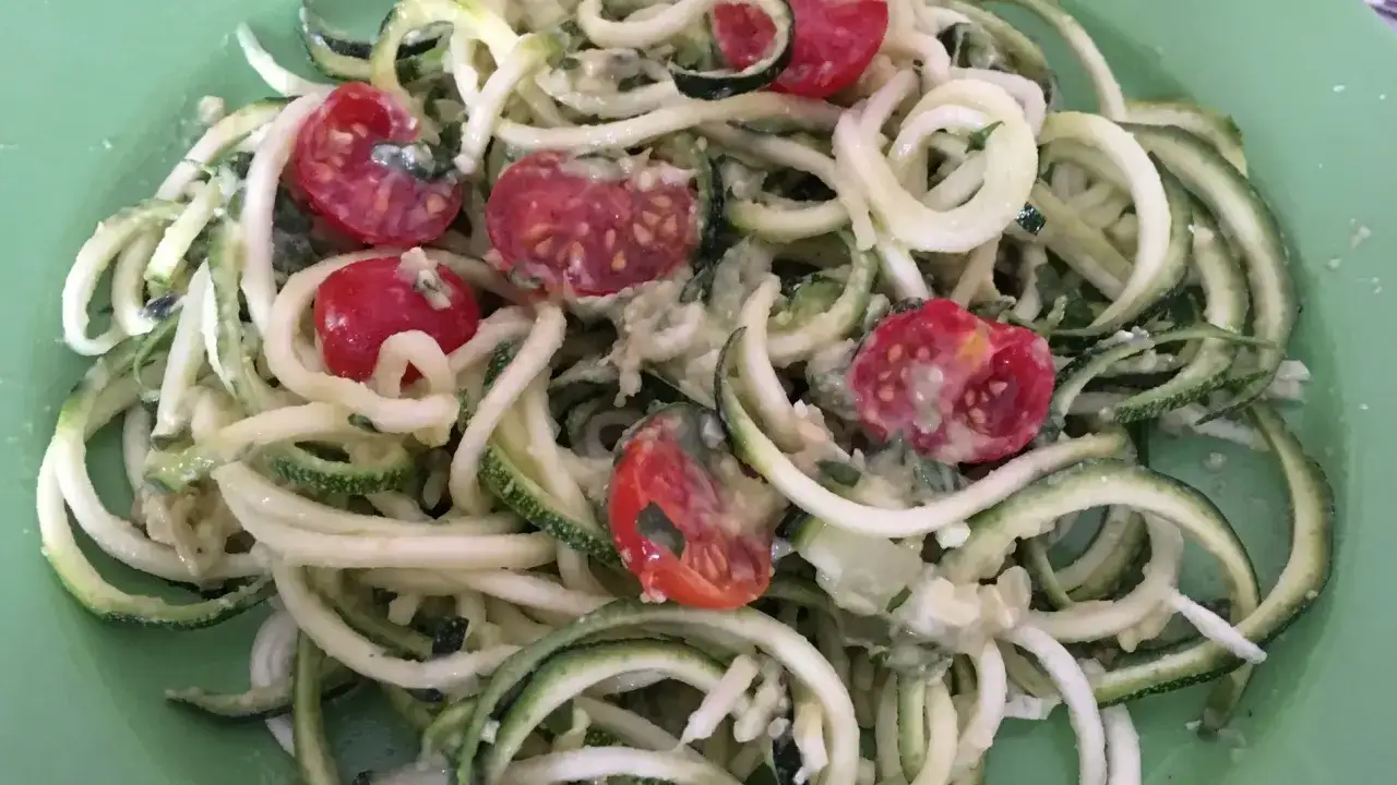 Espaguetis de calabacín con tomates cherry y una cremosa salsa, servidos en un plato verde.