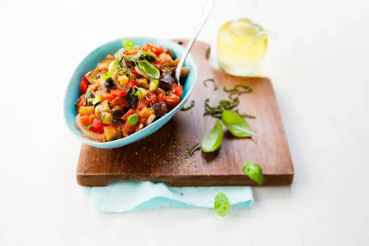 Un d&eacute;licieux ratatouille Cookeo servi dans un bol bleu, garni de basilic frais.