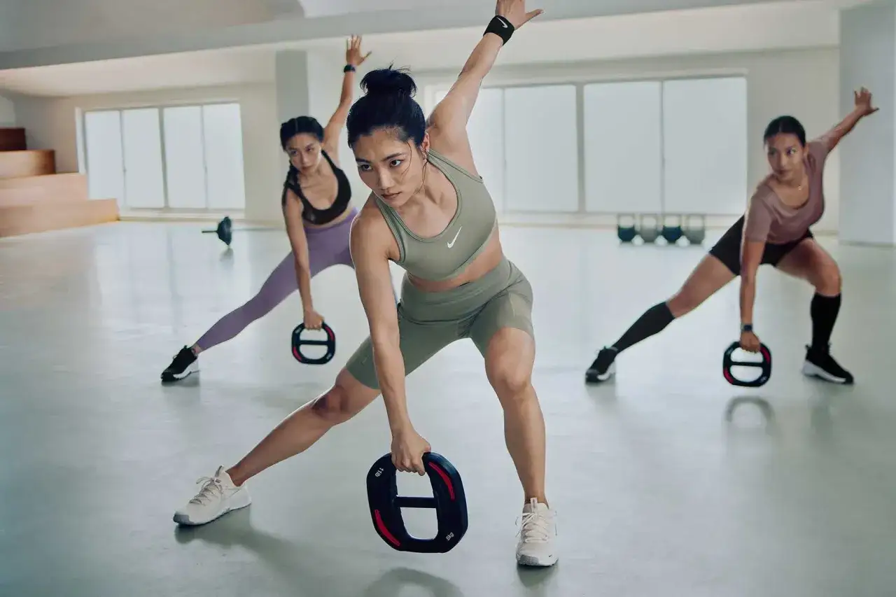 Trois femmes effectuent un exercice cardio en salle, tenant des poids pour un entra&icirc;nement dynamique.