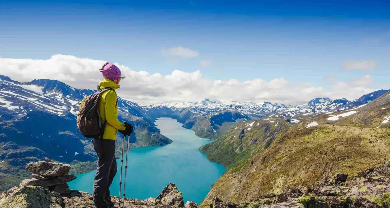 Vandrare njuter av den hisnande utsikten &ouml;ver en turkos sj&ouml; och sn&ouml;kl&auml;dda berg i Jotunheimen nationalpark.