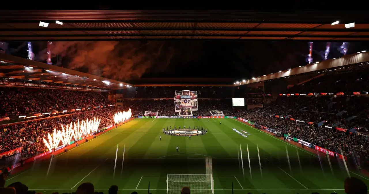 Piłkarze wychodzą na murawę stadionu podczas meczu Premier League, otoczeni pokazami pirotechnicznymi i transparentami kibiców.