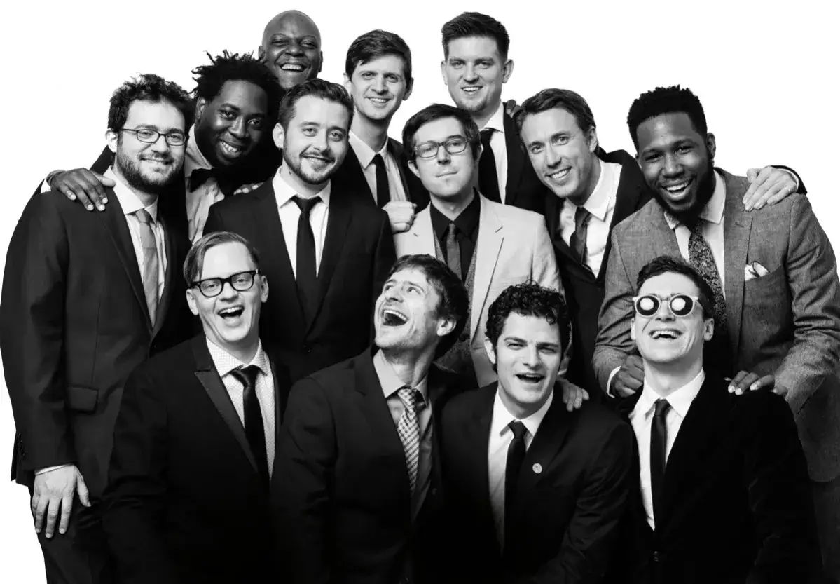 A group of men in suits, possibly the snarky puppy setlist, pose for a photo, all smiling and laughing.