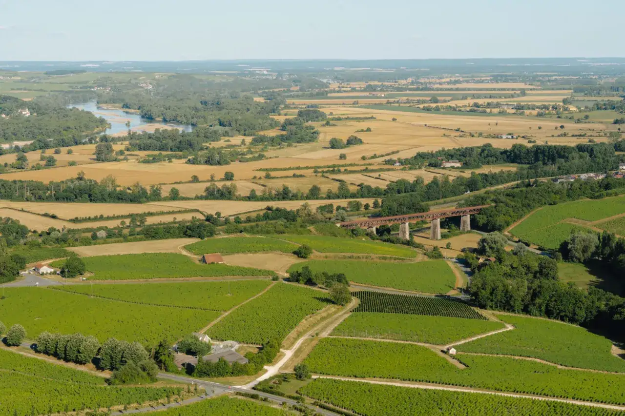Vue a&eacute;rienne des vignobles verdoyants et des champs dor&eacute;s, travers&eacute;s par une rivi&egrave;re et un pont ferroviaire. Un paysage typique du tour des fiefs sancerre.
