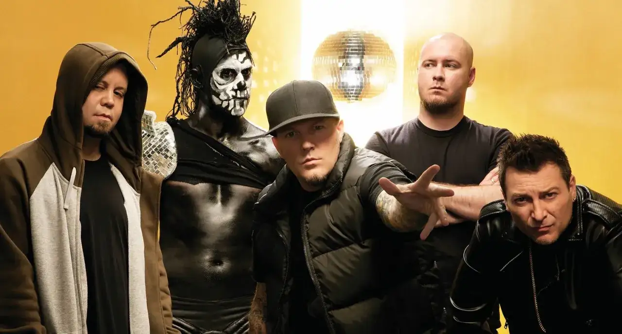 Limp Bizkit członkowie pozują na tle żółtej ściany z dyskotekową kulą.