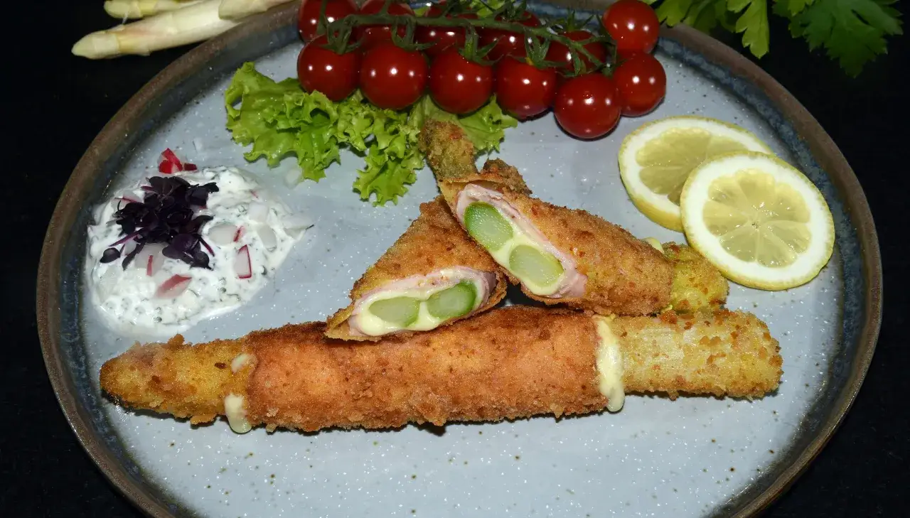 Knuspriges Spargel Cordon Bleu mit Schinken und K&auml;se, serviert mit Dip, Kirschtomaten und Zitrone.