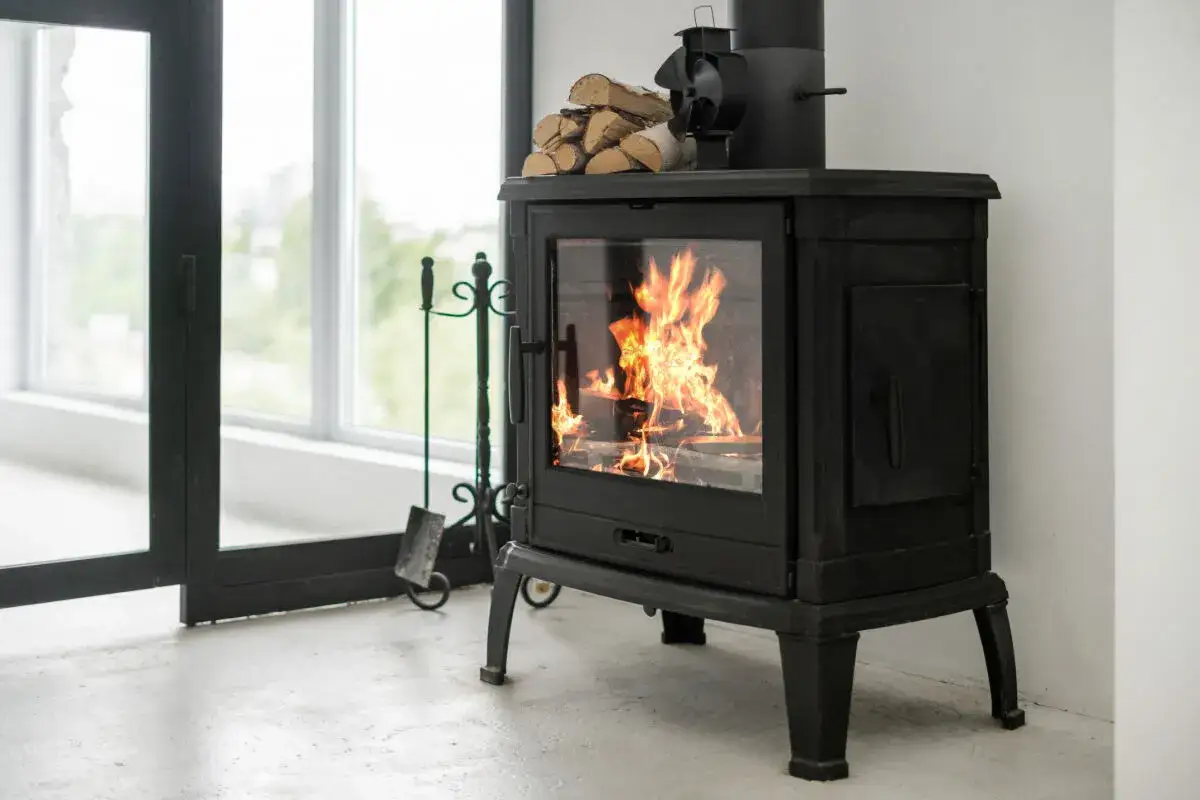 Un feu crépite dans ce cee poele a bois noir, apportant une ambiance chaleureuse. Des bûches attendent sur le dessus.
