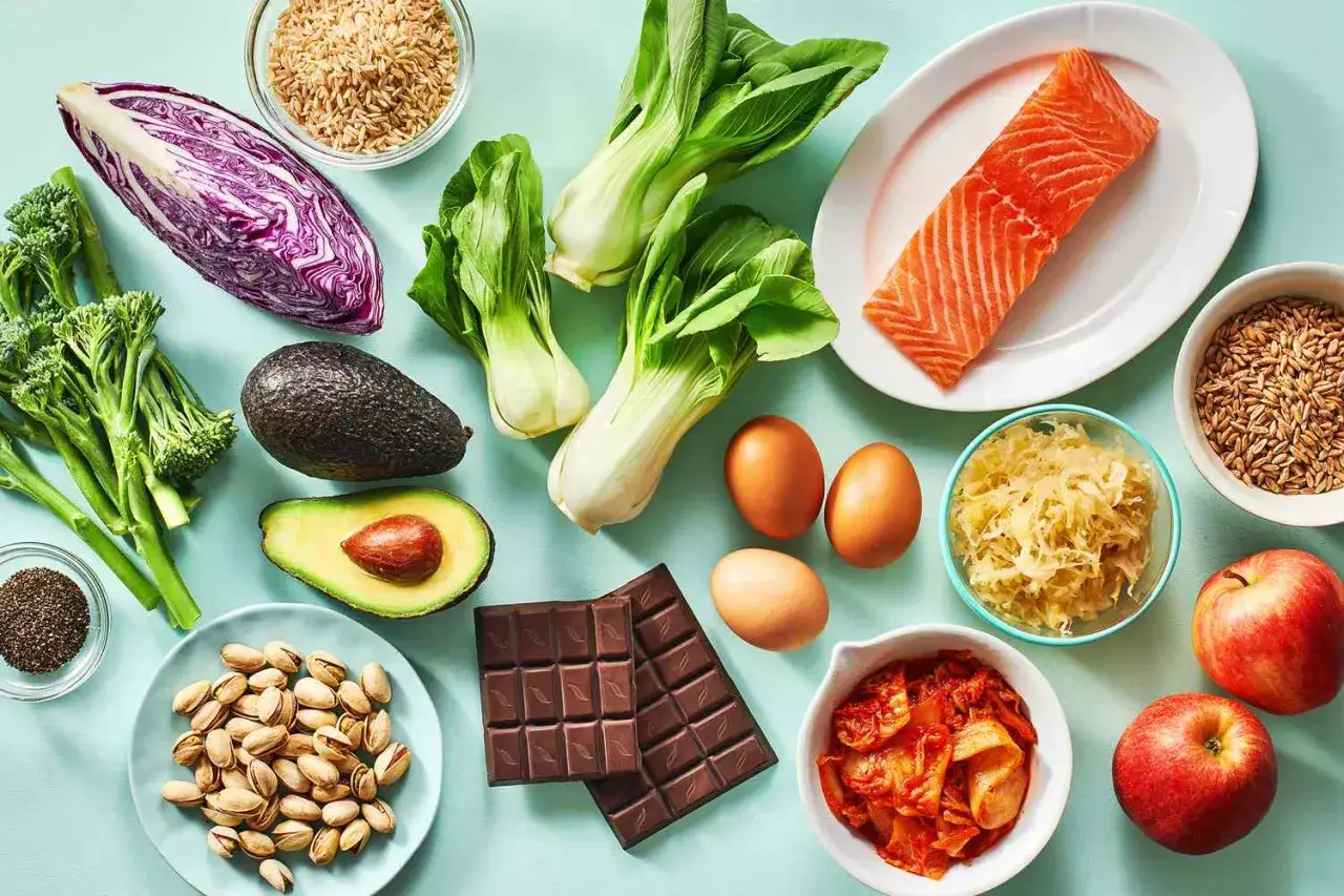 Bunte Auswahl an fettverbrenner lebensmittel: Lachs, Avocado, Brokkoli, Rotkohl, Eier, N&uuml;sse, Schokolade, &Auml;pfel, Kimchi, Sauerkraut und Getreide.