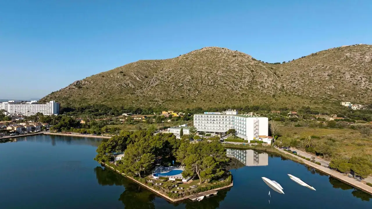 Hotel TUI Suneo Lagomonte z basenem na wyspie, otoczony jeziorem i górami.