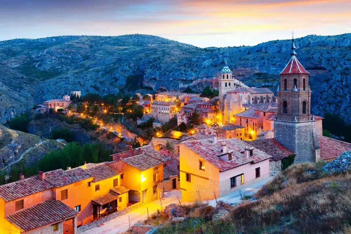 Pueblo español iluminado al atardecer, ideal para viajes fin de semana baratos todo incluido. Casas de tejas rojas y torres de iglesias.