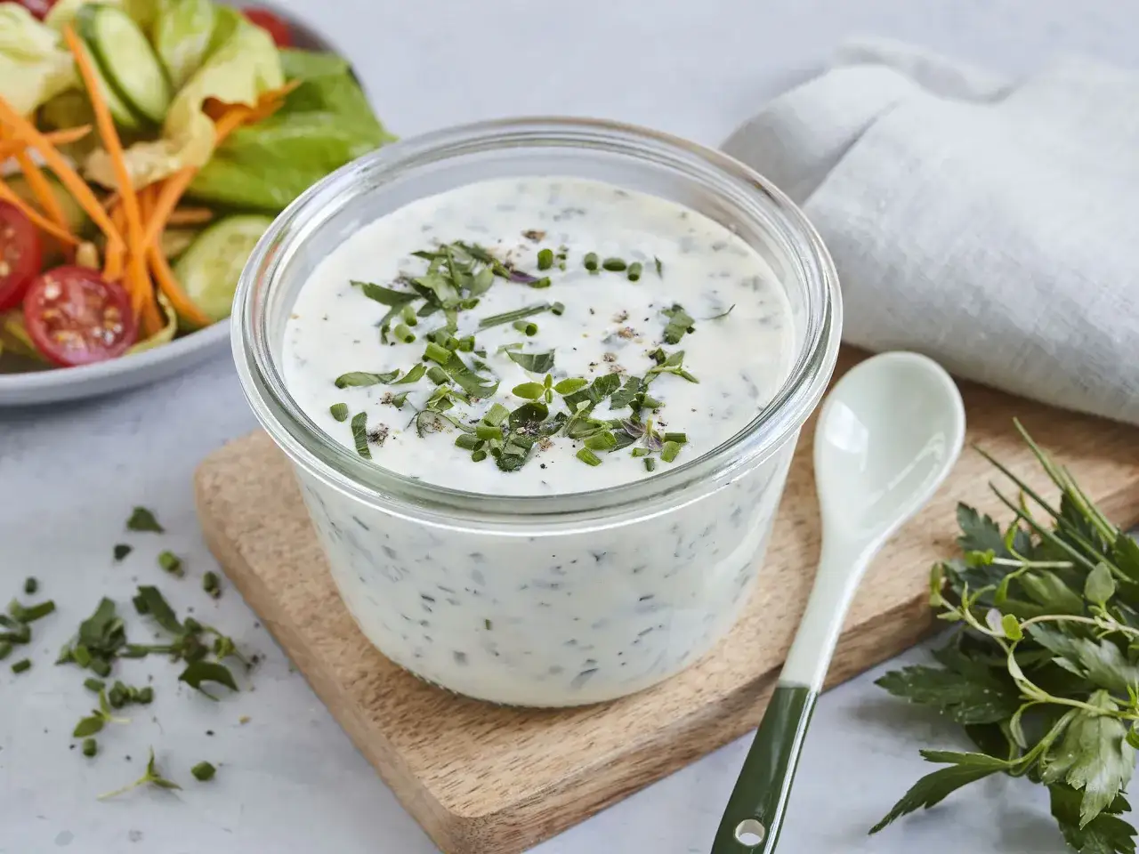 Frisches joghurt dressing mit Kräutern, garniert mit Schnittlauch und Pfeffer. Daneben ein Löffel und ein Salat.
