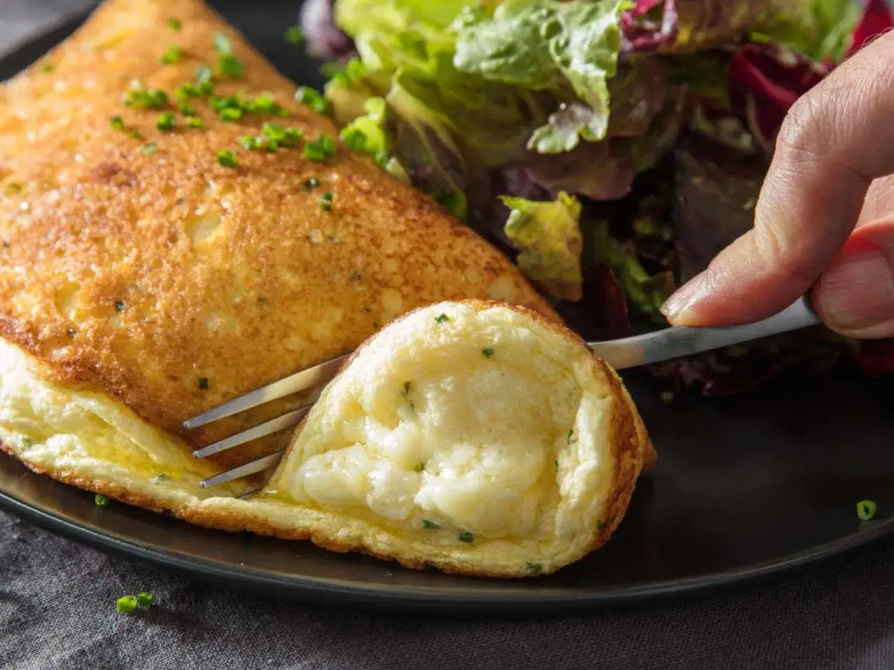 Ein fluffiges Omelett mit Käsefüllung, perfekt für ein schnelles Omelett Rezept. Daneben ein bunter Salat.