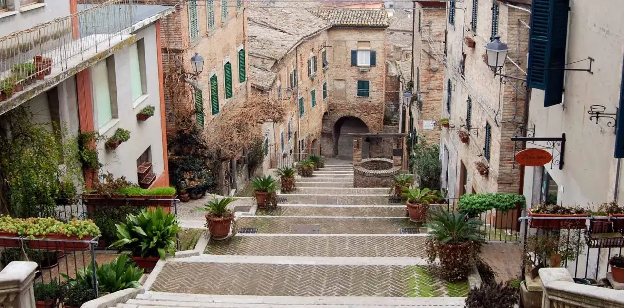 Scalinata fiorita in un borgo delle Marche, tra antiche case in pietra e un pozzo. Un angolo pittoresco che incanta, tra le tante attrazioni Marche.