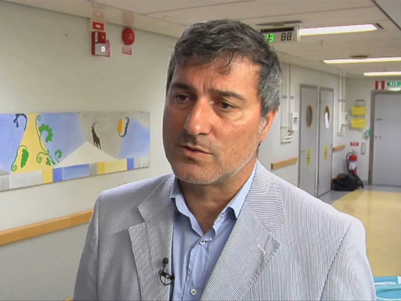 Paolo Macchiarini oggi, in un corridoio ospedaliero, con un quadro astratto alle spalle.