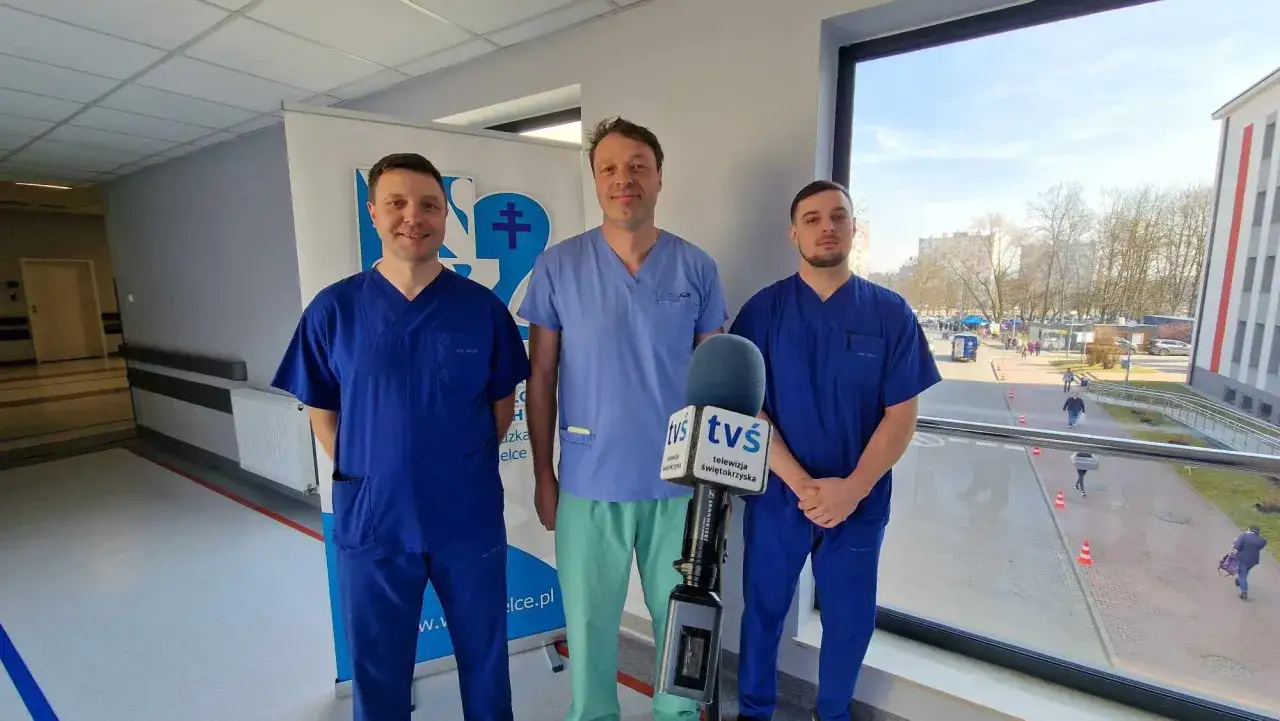 Trzech lekarzy w niebieskich fartuchach stoi przed mikrofonem TVS.