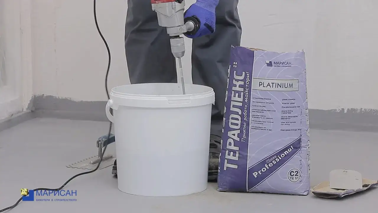 Preparando cemento cola para poner azulejos. Un mezclador eléctrico remueve la mezcla en un cubo blanco junto a un saco de