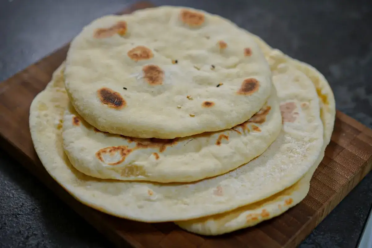 Pile de pains libanais moelleux, légèrement dorés par la cuisson, sur une planche en bois.