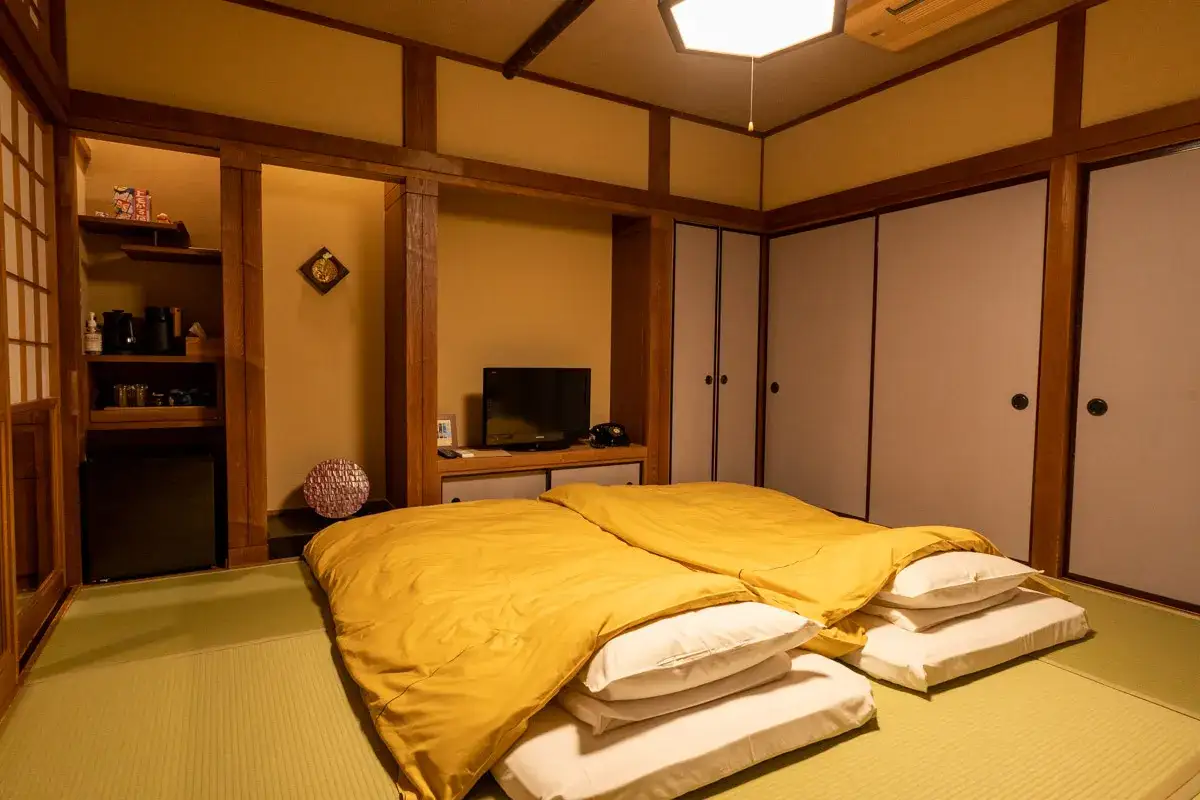 Przytulny pokój w ryokanie z dwoma żółtymi futonami, tatami i tradycyjnymi drzwiami shoji.
