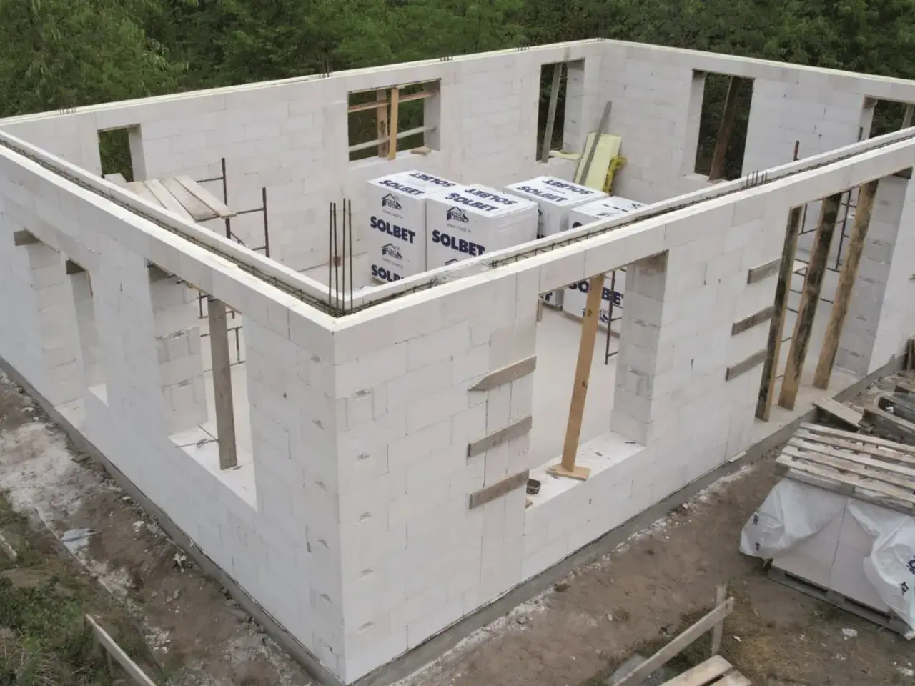 Budowa domu z bloczków z betonu komórkowego. Widoczne ściany z otworami okiennymi i drzwiowymi, materiały budowlane.