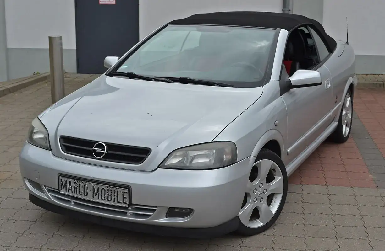 Silberner Opel Astra Bertone Cabriolet mit offenem Verdeck, bereit für eine Spritztour.