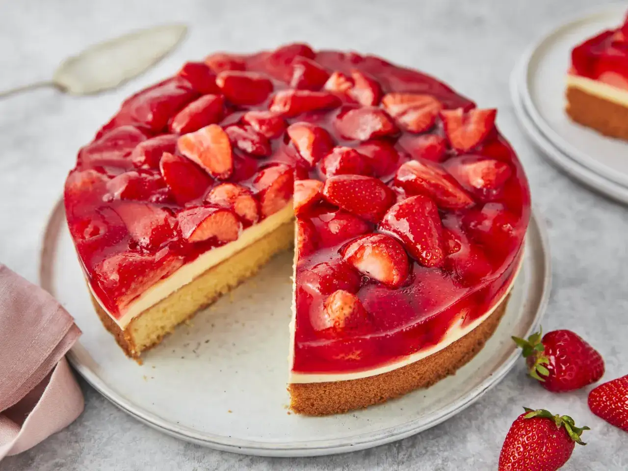 Erdbeerkuchen mit Biskuitboden und Vanillepudding, bedeckt mit frischen Erdbeeren und rotem Tortenguss. Ein St&uuml;ck ist bereits angeschnitten.