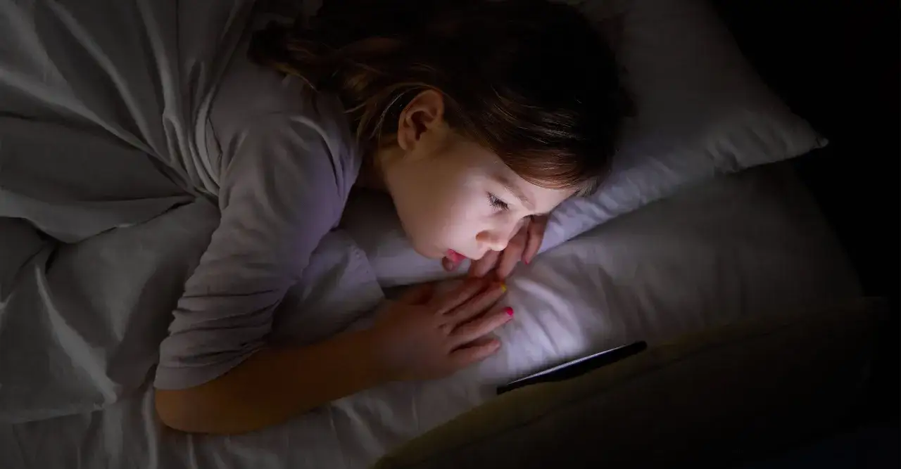 En 8-åring har svårt att somna och tittar på en mobiltelefon i mörkret.