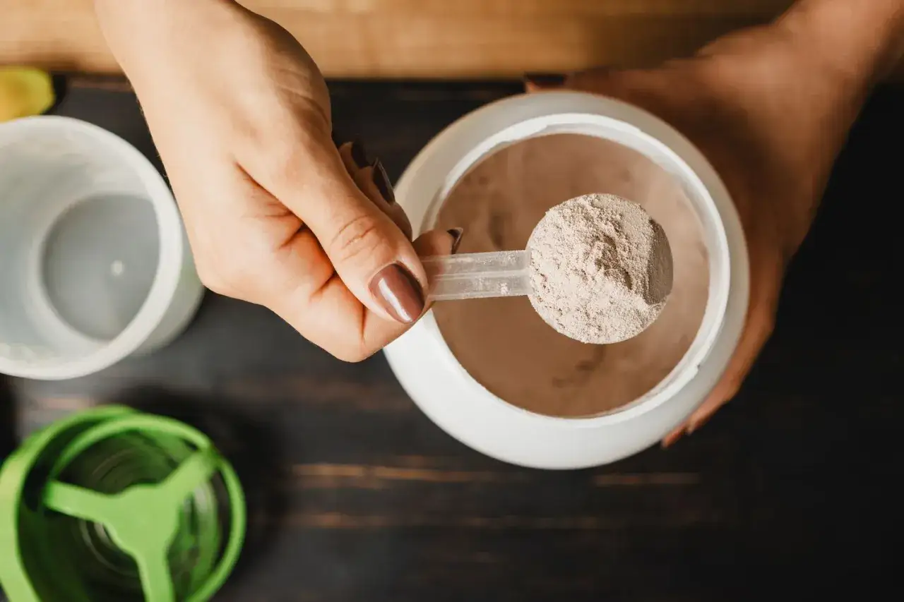 En hand h&aring;ller en skopa med proteinpulver. Fr&aring;gan om hur mycket kreatin per dag &auml;r relevant f&ouml;r att optimera tr&auml;ningen.