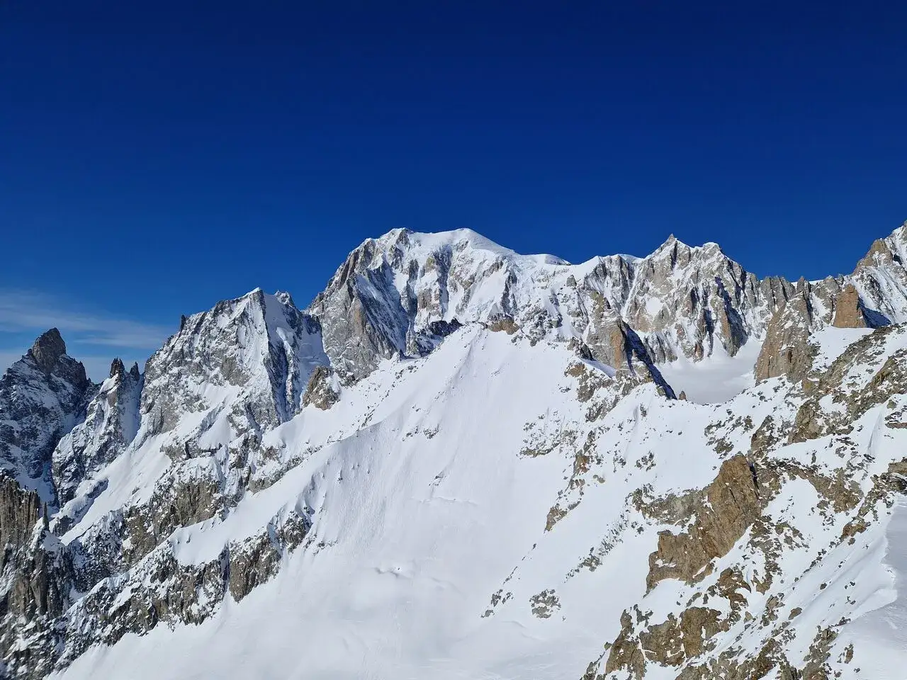 Majestatyczny Mont Blanc w śnieżnej koronie, pod błękitnym niebem. Skaliste zbocza i lodowce tworzą zapierający dech w piersiach krajobraz.