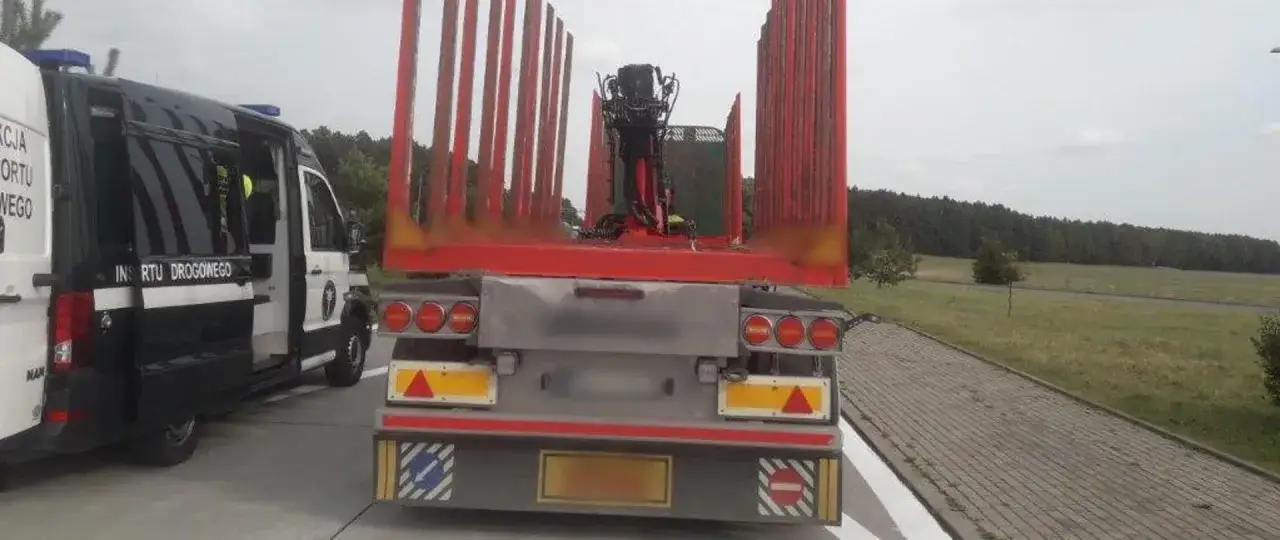 Inspekcja Transportu Drogowego sprawdza dopuszczalną masę całkowitą zespołu pojazdów. Ciężarówka z drewnem i dźwigiem stoi obok radiowozu.
