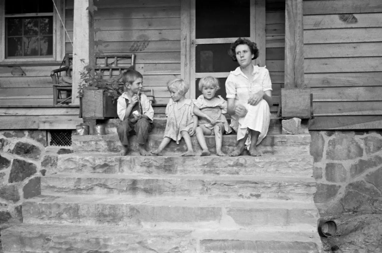 A mother and three children sit on stone steps in this Arthur Rothstein photo. The children look toward the viewer, while the mother gazes away.