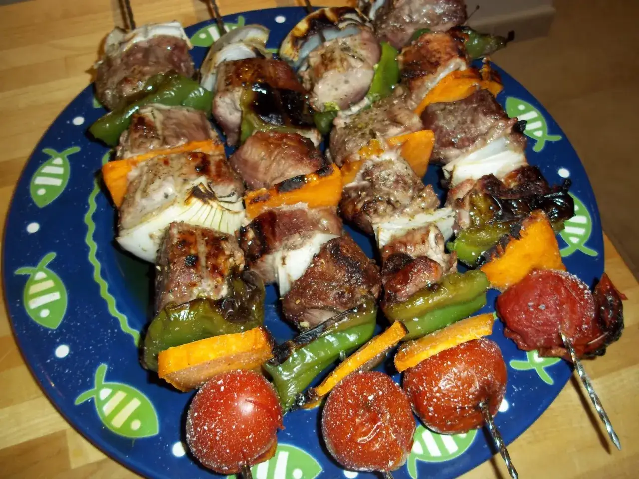 Brochetas de solomillo con pimientos verdes, cebolla y calabaza asados, servidas en un plato azul con dibujos de peces.