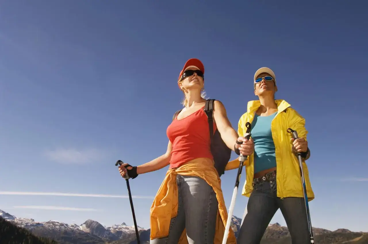 Dwie kobiety cieszą się pięknym dniem, uprawiając **nordic walking** wśród gór.