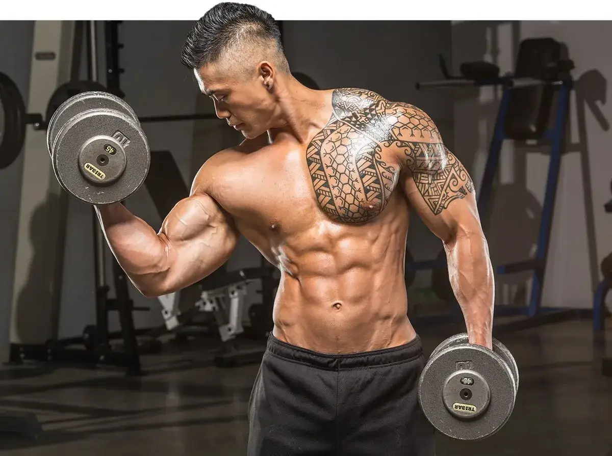 Mężczyzna z tatuażami wykonuje ćwiczenia na biceps z hantlami. To najlepsze ćwiczenia na biceps dla imponującej masy mięśniowej.